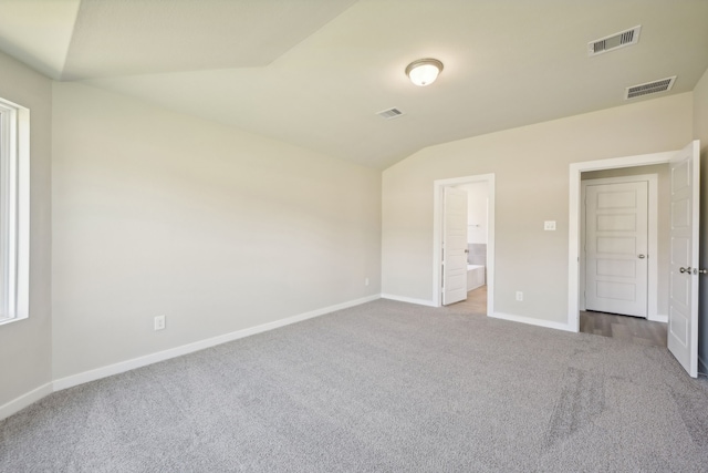 unfurnished bedroom featuring vaulted ceiling, light colored carpet, and ensuite bath