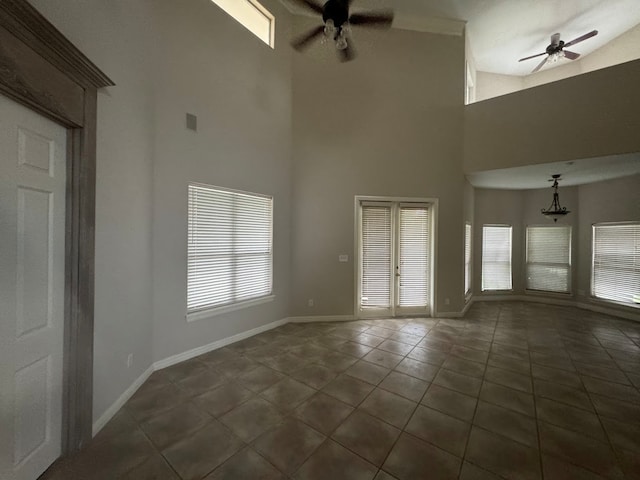 interior space featuring dark tile patterned flooring, ceiling fan with notable chandelier, a high ceiling, and a wealth of natural light