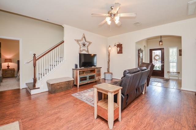 living room featuring wood-type flooring, crown molding, and ceiling fan