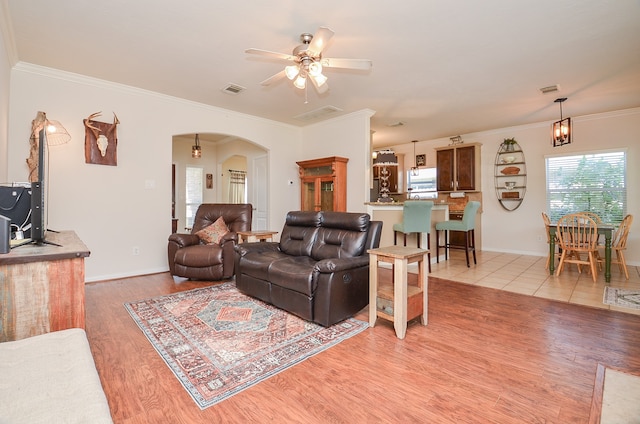 living room featuring ceiling fan with notable chandelier, ornamental molding, and light hardwood / wood-style flooring