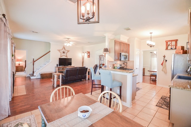 dining room featuring ceiling fan with notable chandelier, light wood-type flooring, ornamental molding, and sink