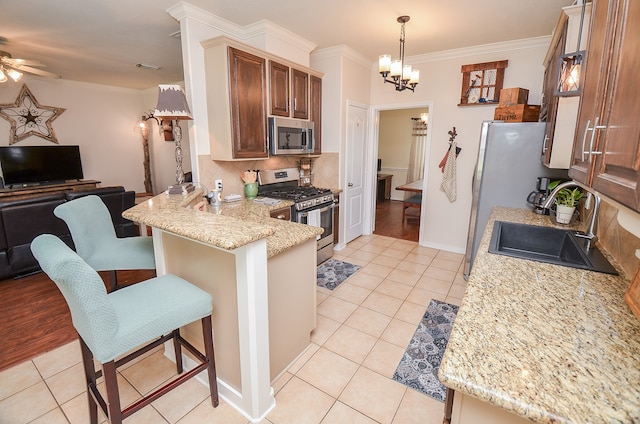 kitchen featuring a kitchen breakfast bar, ceiling fan with notable chandelier, kitchen peninsula, stainless steel appliances, and sink