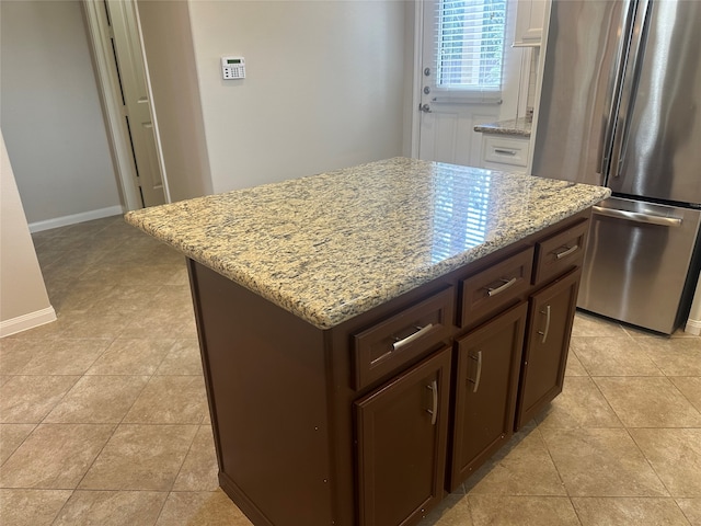 kitchen featuring stainless steel fridge, light tile patterned flooring, light stone counters, a center island, and dark brown cabinetry