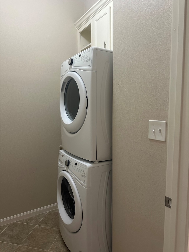 clothes washing area featuring stacked washer and clothes dryer, dark tile patterned floors, and cabinets