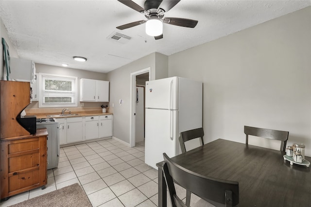 kitchen with ceiling fan, light tile patterned floors, stove, white fridge, and white cabinets