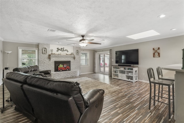 living room featuring ornamental molding, a textured ceiling, ceiling fan, dark wood-type flooring, and a fireplace