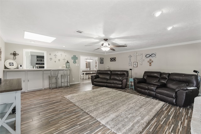 living room with ceiling fan, ornamental molding, dark wood-type flooring, and a skylight