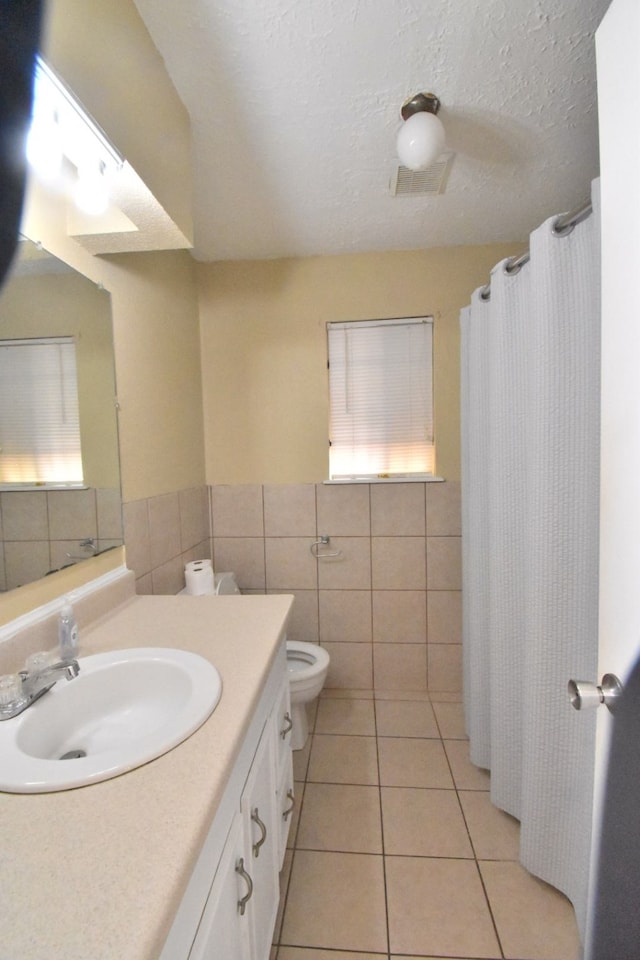 bathroom with tile walls, tile patterned flooring, a textured ceiling, vanity, and toilet