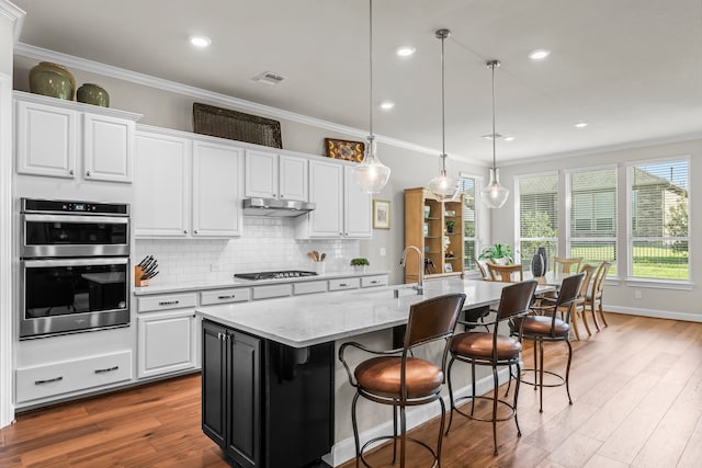 kitchen with an island with sink, crown molding, and white cabinetry