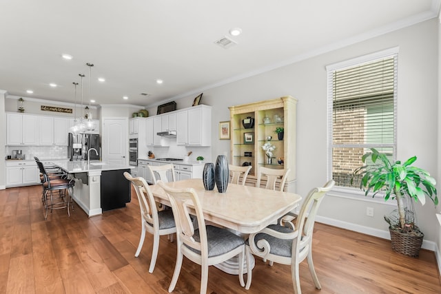 dining area with wood-type flooring, crown molding, and sink