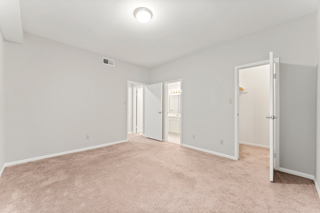 unfurnished bedroom with ensuite bath, a spacious closet, a closet, and light colored carpet