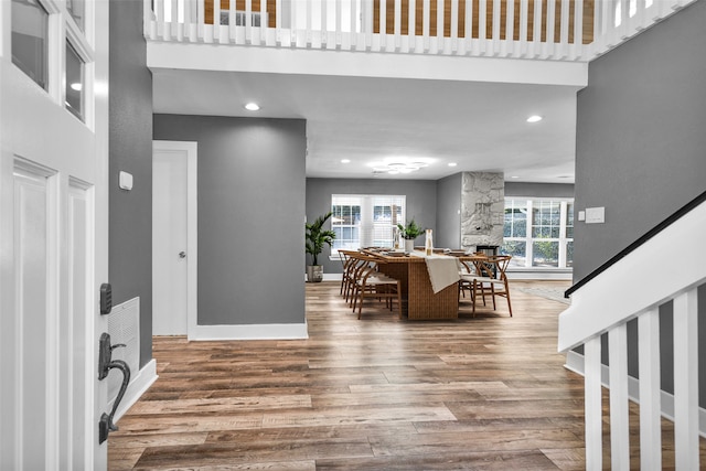 entrance foyer featuring a wealth of natural light, a towering ceiling, wood-type flooring, and a fireplace