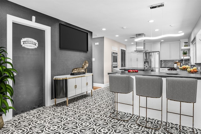 kitchen featuring white cabinetry, a breakfast bar, kitchen peninsula, island range hood, and stainless steel appliances