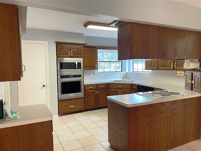 kitchen with stainless steel appliances, kitchen peninsula, light tile patterned flooring, and a textured ceiling