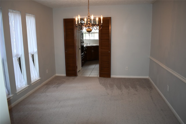 unfurnished dining area featuring light carpet, a textured ceiling, sink, and a chandelier