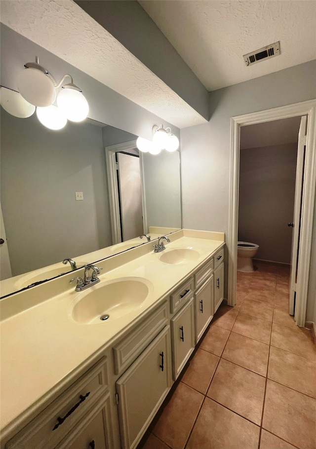 bathroom with a textured ceiling, tile patterned flooring, vanity, and toilet