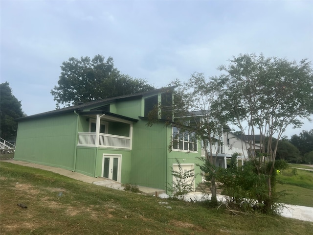 view of side of property featuring a balcony, french doors, and a yard