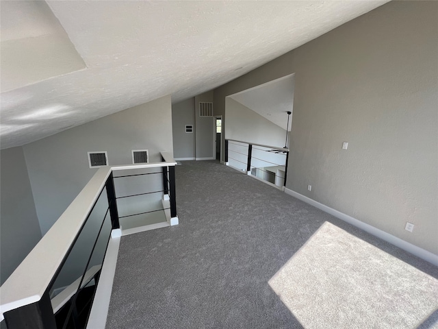 additional living space with a textured ceiling, lofted ceiling, and dark colored carpet