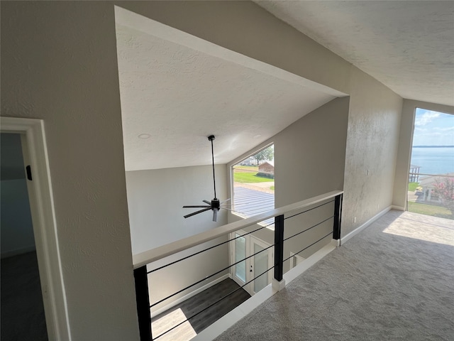 stairs featuring a water view, vaulted ceiling, a textured ceiling, ceiling fan, and carpet