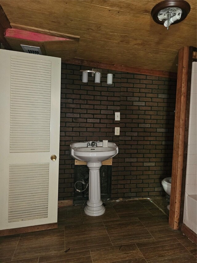 bathroom featuring wood ceiling, brick wall, and toilet