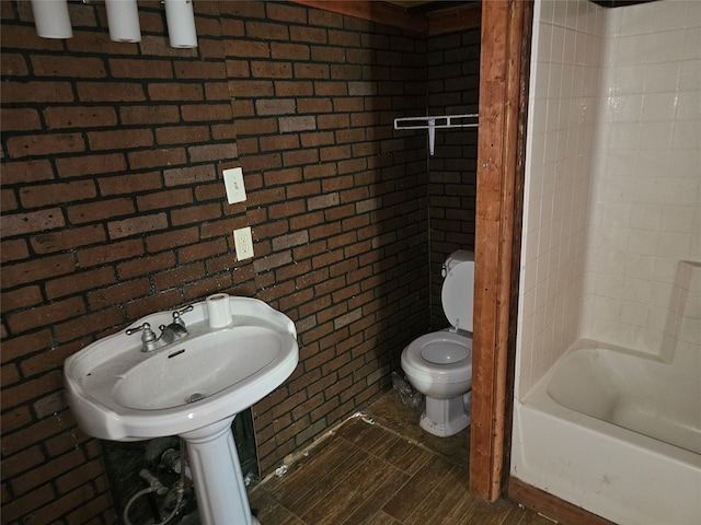 bathroom with brick wall, toilet, and shower / bathtub combination