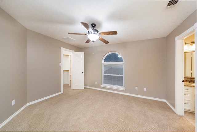 unfurnished bedroom featuring light carpet, ceiling fan, ensuite bathroom, and a textured ceiling