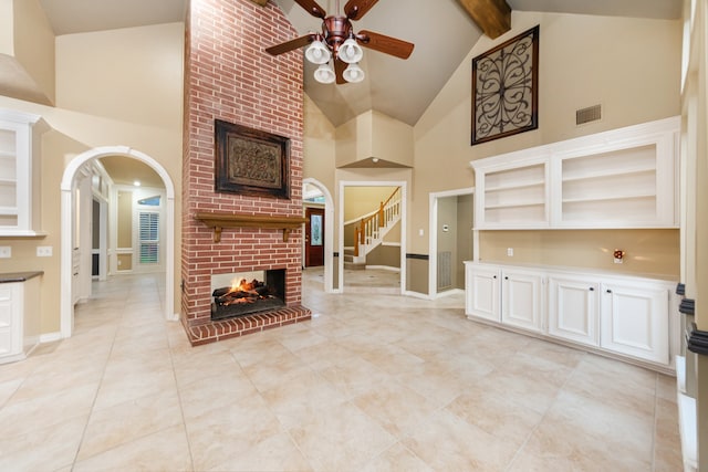 unfurnished living room with ceiling fan, built in shelves, beamed ceiling, a brick fireplace, and high vaulted ceiling