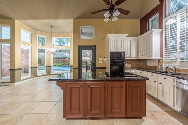 kitchen with plenty of natural light, dark stone counters, white cabinetry, a center island, and ceiling fan with notable chandelier