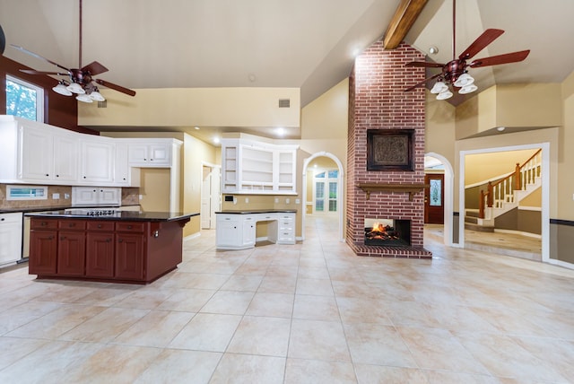 kitchen featuring ceiling fan, beam ceiling, high vaulted ceiling, white cabinetry, and a fireplace