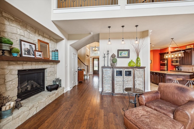 living room featuring a high ceiling, a stone fireplace, dark wood-type flooring, and a chandelier