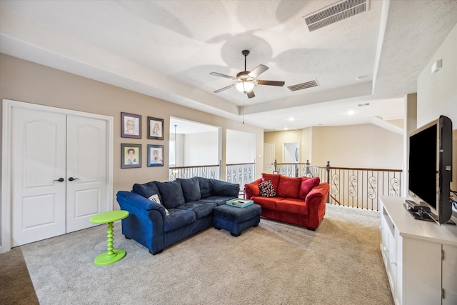 carpeted living room featuring a textured ceiling, a tray ceiling, and ceiling fan