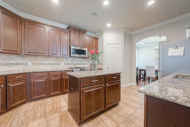 kitchen with appliances with stainless steel finishes, backsplash, crown molding, and a kitchen island