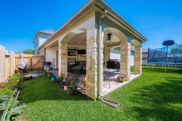 rear view of property featuring a trampoline, a lawn, ceiling fan, and a patio