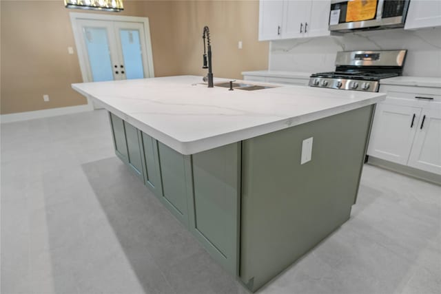 kitchen featuring light stone countertops, a center island with sink, appliances with stainless steel finishes, and white cabinetry