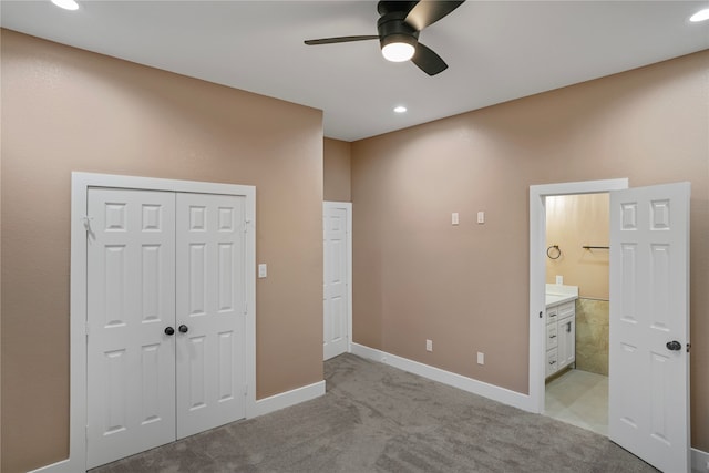 unfurnished bedroom featuring light carpet, a closet, ensuite bathroom, and ceiling fan