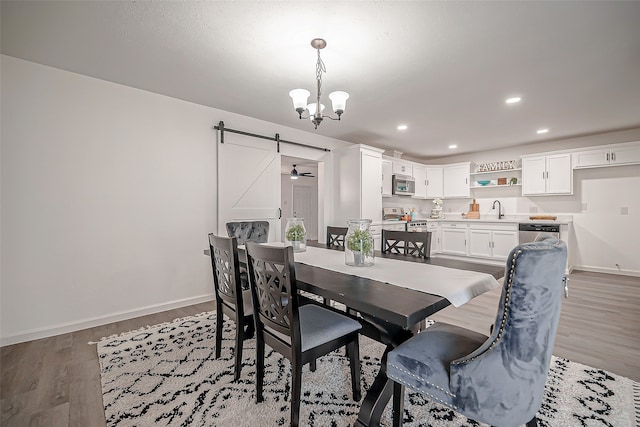 dining space with ceiling fan with notable chandelier, sink, hardwood / wood-style flooring, and a barn door