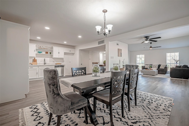 dining space with ceiling fan with notable chandelier, sink, and light hardwood / wood-style flooring