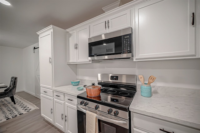 kitchen featuring light stone countertops, stainless steel appliances, white cabinets, and light wood-type flooring