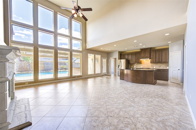 unfurnished living room featuring ceiling fan, a towering ceiling, a high end fireplace, and plenty of natural light