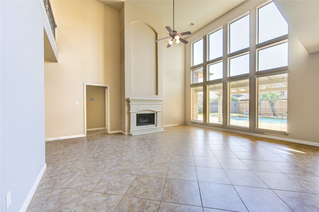 unfurnished living room featuring ceiling fan, a towering ceiling, and light tile patterned floors