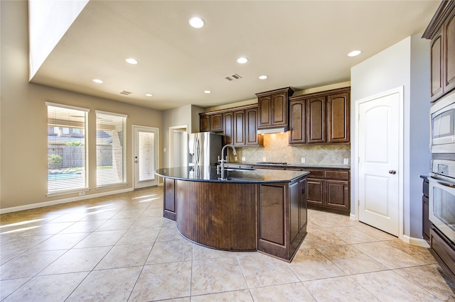 kitchen featuring light tile patterned flooring, sink, stainless steel appliances, backsplash, and a center island with sink