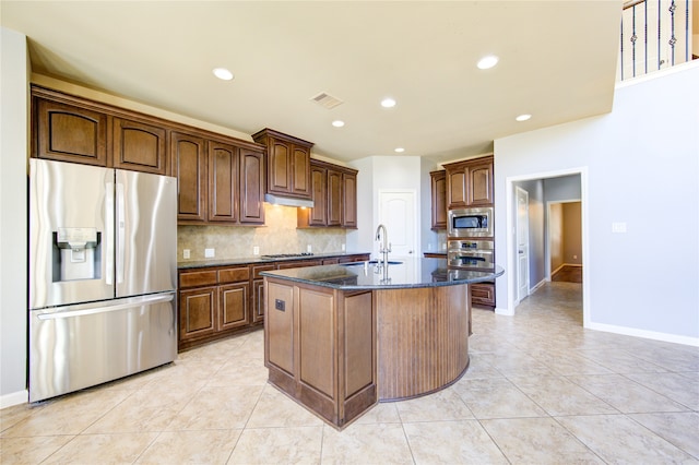 kitchen with dark stone counters, tasteful backsplash, sink, an island with sink, and stainless steel appliances