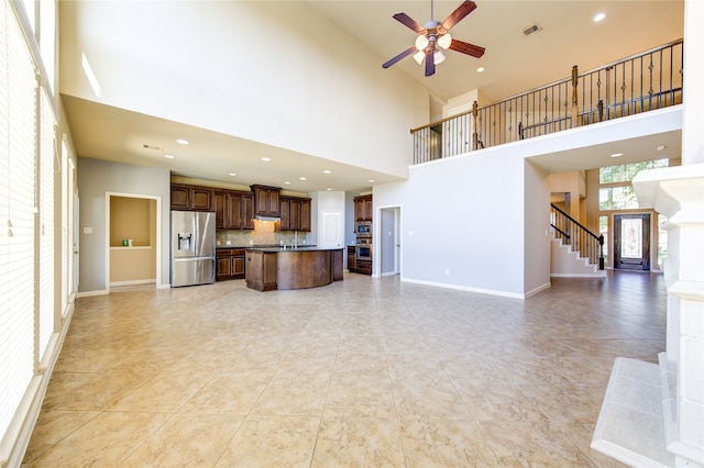 unfurnished living room with light tile patterned floors, a towering ceiling, ceiling fan, and a fireplace