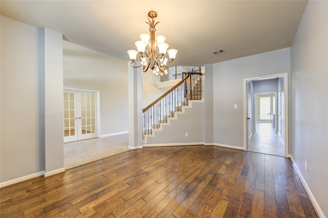 spare room with an inviting chandelier, dark hardwood / wood-style floors, and french doors