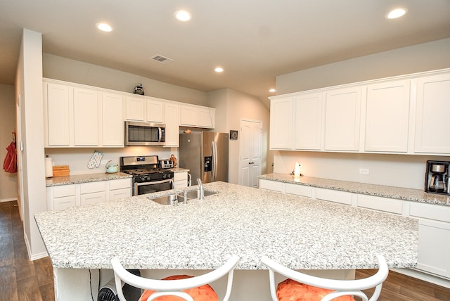 kitchen with a breakfast bar area, a kitchen island with sink, stainless steel appliances, and dark hardwood / wood-style flooring