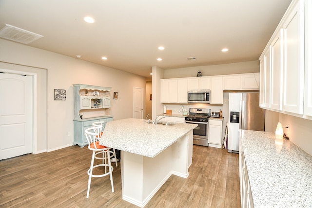 kitchen featuring light stone countertops, light hardwood / wood-style floors, appliances with stainless steel finishes, and a center island with sink