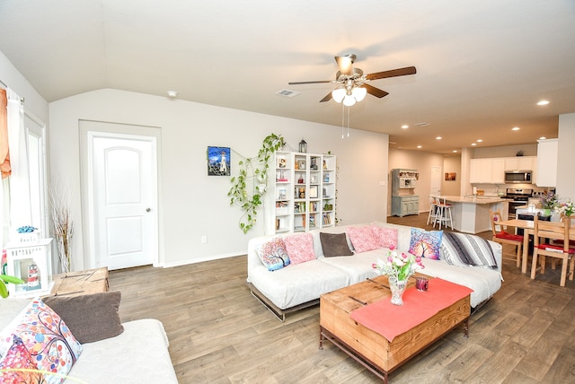 living room featuring ceiling fan, vaulted ceiling, and light hardwood / wood-style floors