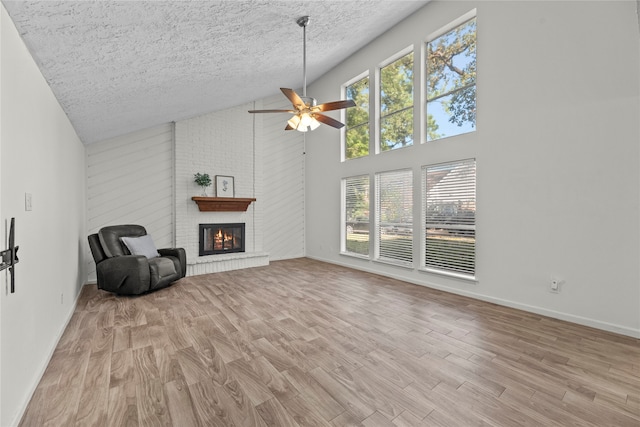 living room with light hardwood / wood-style floors, a brick fireplace, high vaulted ceiling, a textured ceiling, and ceiling fan