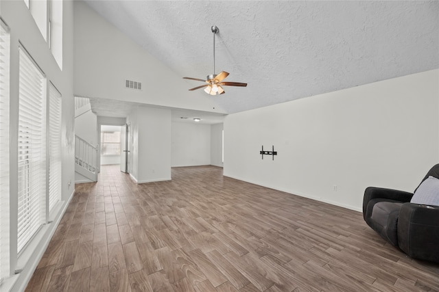 unfurnished living room with light wood-type flooring, a textured ceiling, ceiling fan, and high vaulted ceiling