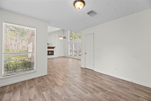 unfurnished room featuring a large fireplace, ceiling fan, and a wealth of natural light